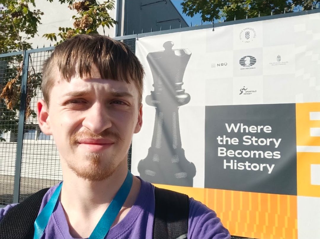 Attila at a chess event in front of a giant queen and the banner line “Where the Story Becomes History”